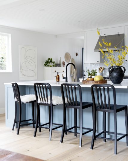 a custom kitchen renovation featuring black chair, blue cabinetry, floating wooden shelves, herringbone tile backsplash and a big window letting in lots of light